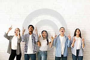 Group of Multiethnic Teenagers Pointing Upwards Against White Brick Wall