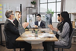 Group of multiethnical businesspeople clapping hands and looking at screen, having video conference