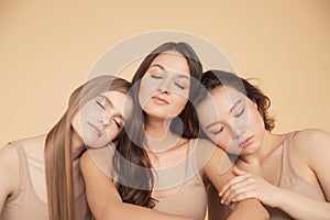 Group multiracial beauty smiling women with perfect face hug and looking camera. Concept spa skin care beige background