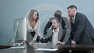 Group of multiracial business people around the conference table looking at laptop computer and talking to one another