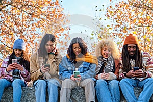 Group of multiracial friends using smart mobile phone device outdoors in autumn.