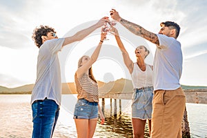 Group of multiracial happy friends toasting at the beach with red wine at sunset clinking glasses in front of sunlight in backlit