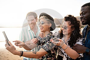 Group of multiracial happy young friends laughing, taking selfie with mobile phone, having fun together on the beach. Multi ethnic
