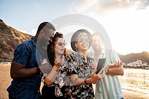 Group of multiracial happy young friends laughing, watching something funny in social media on mobile phone, having fun together
