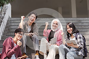 A group of multiracial and happy young people are raising their hands in celebration having fun together while sitting