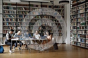 Group of multiracial students sit at table in library