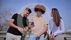 Group of multiracial teenage friends having fun using a cellphone device outdoors. Three multiethinc young people