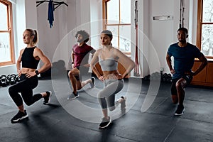 Group of multiracial young adults doing lunges with hands on hips at the gym