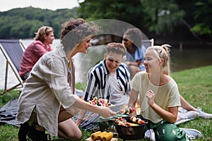 Group of multiracial young friends camping in campsite near lake and and having barbecue together.