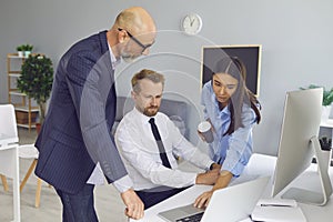 Group of office workers business colleagues or partners looking at laptop screen and discussing project