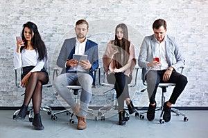 A group ofpeople, in the waiting room and each spending time. Indoors.