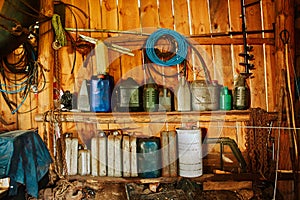 A group of old canisters and cylinders stand on shelves in a wooden shed