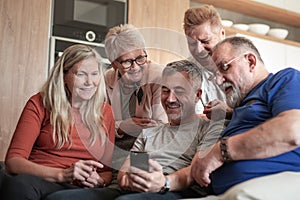 Group of older friends with a smartphone sitting in a cozy living room.