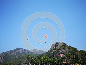 A group of parachuters flying high above a green hill in the summertime blue sky, Fethiye, Mugla