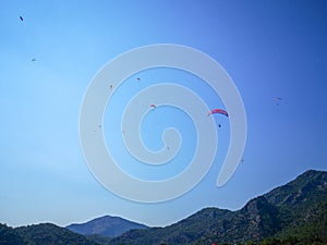 A group of parachuters flying high above a green hill in the summertime blue sky, Fethiye, Mugla