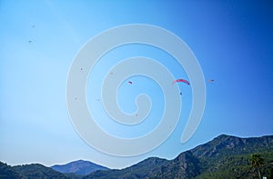 A group of parachuters flying high above a green hill in the summertime blue sky, Fethiye, Mugla