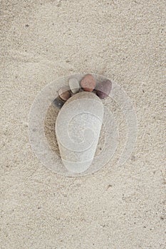 Group of pebble stones on sand creating de form of a foot in isolated white background