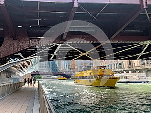 Group of pedestrians enjoy the riverwalk as water taxis pass each other on the Chicago River