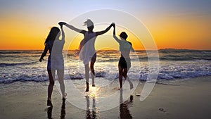 Group of people on the beach in sunset holding for hands having fun