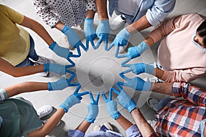 Group of people in blue medical gloves joining fingers indoors, top view
