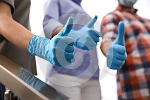 Group of people in blue medical gloves showing thumbs up on light background, closeup