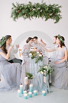 Group of people bride and groom, bridesmaids and groommen sitting at wedding table with wedding cake, pine decoration