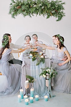 Group of people bride and groom, bridesmaids and groommen sitting at wedding table with wedding cake, pine decoration