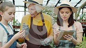 Group of people child mother and granny talking and making notes working in greenhouse together