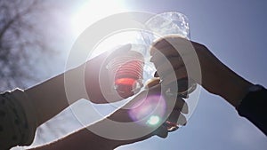 A group of people clinking glasses of beautiful glass with drinks against the sky and sun with a lens effect. HD