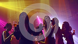 Group of people dance in disco night club to the beat of music from DJ on stage