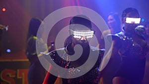 Group of people dance in disco night club to the beat of music from DJ on stage