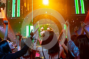 Group of people dance in disco night club to the beat of music from DJ on stage