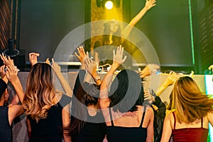 Group of people dance in disco night club to the beat of music from DJ on stage