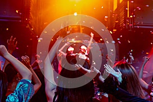 Group of people dance in disco night club to the beat of music from DJ on stage