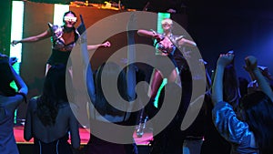Group of people dance in disco night club to the beat of music from DJ on stage