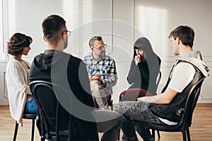 Group of people of different ages sits in a circle during a meeting with a professional therapist photo