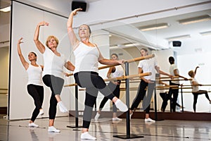 Group of people doing exercises using barre in gym with focus to fit athletic toned woman in foreground in health