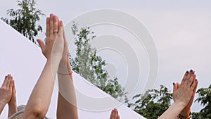 Group of people doing yoga exercises - raising hands up in namaste mudra at park