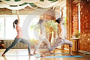 group of people doing yoga warrior pose at studio