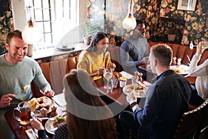 Group Of People Eating In Restaurant Of Busy Traditional English Pub