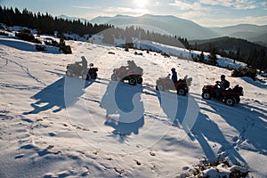 Group of people enjoying sunset, on off-road four-wheelers ATV bikes on snow in the the mountains in winter