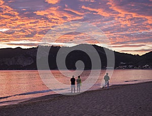 Group of people flying a drone during beautiful blue pink orange clouds sunset on Agios Georgios Pagon beach at Corfu