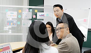 A group of people are gathered around a table with a whiteboard behind them. They are discussing something important, and one of