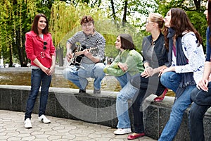 Group people with guitar in city park listen music