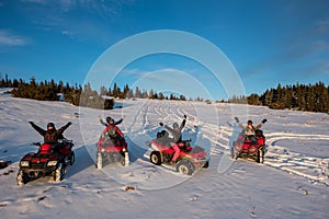 Group of people with hands up on four-wheelers ATV bikes in the the mountains in winter evening