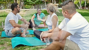 Group of people holding bottle of water sitting on yoga mat at park