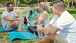 Group of people holding bottle of water sitting on yoga mat at park