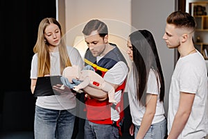 Group of people learning how to make first aid with dummy child during the training indoors
