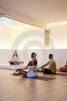 A group of people are meditating, sitting on yoga mats in a room.