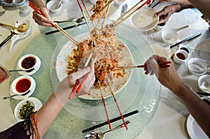 A group of people mixing and tossing Yee Sang dish with chop sticks.